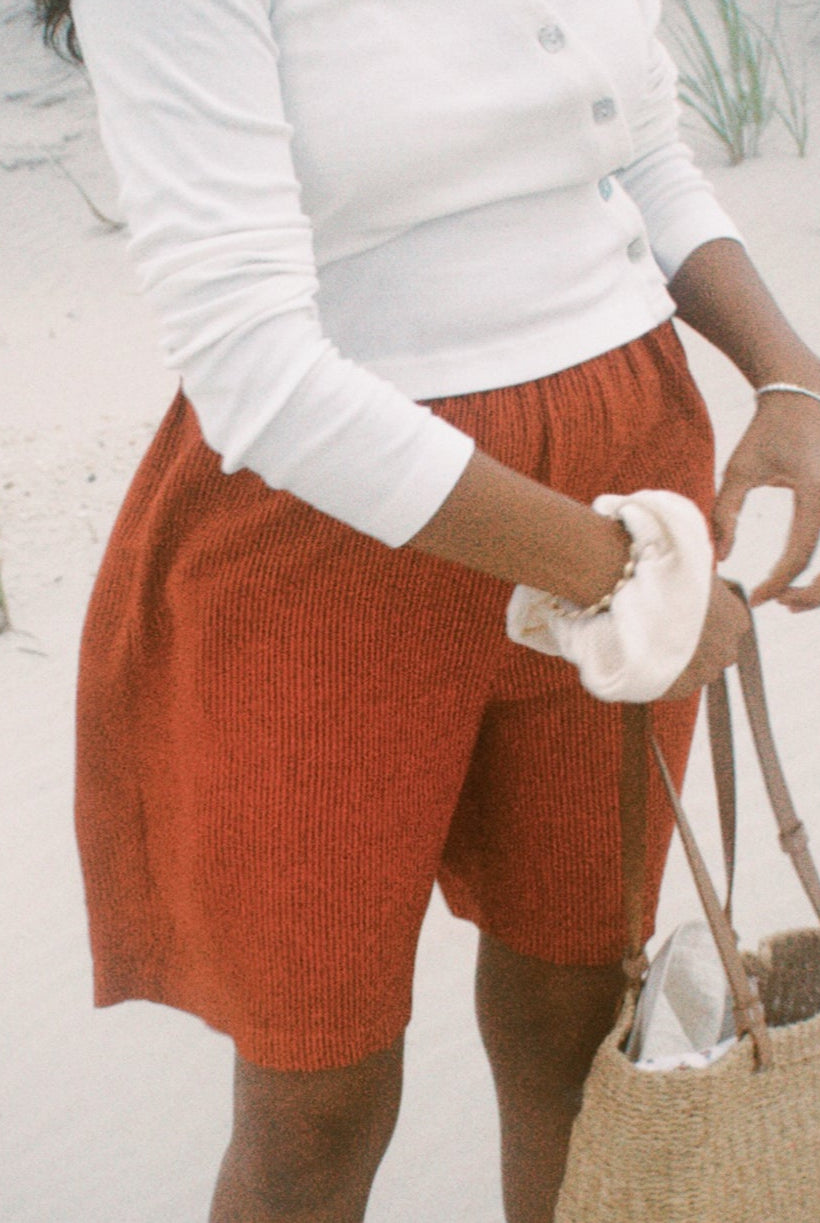 Person wearing a white long-sleeve top and orange shorts on a sandy background